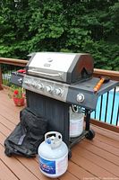 Front view of grill on deck with black cover rolled and extra propane tank in front