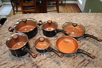 Full view of Farberware Glide ceramic nonstick cookware set with lids, including saucepans and frying pans on a kitchen counter.