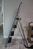 Side view of a four-step folding metal ladder placed indoors against a white wall.