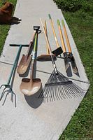All eight garden tools laid out on concrete with grass border, showing full lengths and condition