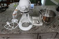 Front view of white tilt-head mixer on counter with bowl and attachments