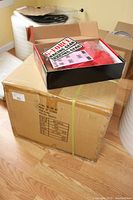 Large cardboard box labeled G-Force containing the jackets, placed on wood floor.