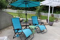 Two blue zero gravity chairs set on concrete patio with matching blue umbrella and small green fold-up table