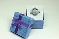 Image of ring displayed in open blue presentation box with purple ribbon bow on top next to it.
