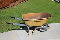 Side view of the yellow True Temper wheelbarrow on concrete with grass background showing overall condition and wear.