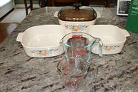 shows 3 Corning Ware casserole dishes (2 rectangular with fruit floral pattern, 1 round with amber lid) and stacked glass measuring cups
