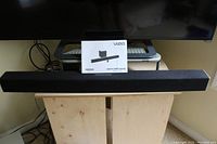 Photo of a VIZIO soundbar placed on a wooden surface with a quick start guide standing upright behind it.