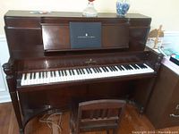 Front view of walnut upright piano with bench, keyboard exposed, Steinway & Sons fallboard logo visible