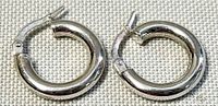 Pair of small white gold hoop earrings lying flat, showing rounded shape and hinged clasp.