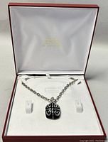 Necklace with pendant displayed in a red box with white interior, showing chain laid out and pendant centered.