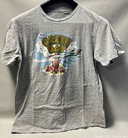 Full front view of the grey Green Day T-shirt with colorful cartoon graphic featuring an aircraft, clouds, and mushroom cloud explosion.