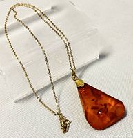 Full view of the gold-tone chain necklace with amber pendant displayed on a clear stand.