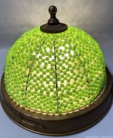 Close up of the light on showing illuminated green beads and metal frame with floral embossing.