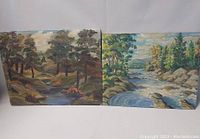 Photo showing two signature oil on board paintings depicting forest and river scenes, signed by Lawrence Smith and H.A.W.