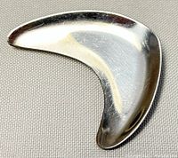 Front view of vintage stainless steel brooch on gray fabric background showing curved shape and reflective surface.