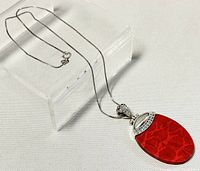 Close-up angled photo of the silver chain necklace with red coral oval pendant displayed on a transparent block against a white background.