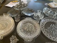 Top-down view of multiple round and tiered pressed glass serving dishes including large platter and divided dish, showing intricate star and circle patterns typical of EAPG glass.
