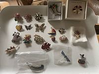Overhead photo showing a collection of vintage brooches arranged on a tray including a boxed Anne Klein bell brooch and a boxed crystal boot brooch.