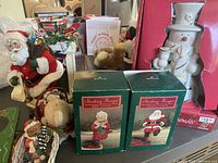 Photo showing Santa musical figurine with a snow globe, two green boxed Stocking Hanger ornaments, and other small figurines including a light-up snowman in the original packaging.