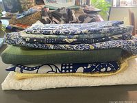 Stack of seven pieces of fabric showing various colors and patterns including blues, greens, yellows, and white lace