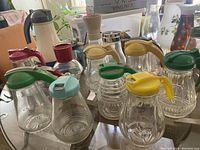 Image showing assorted vintage syrup dispensers with various colored lids, coffee grinder, and pitchers on a table.