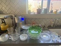 Full view of antique glass collection including footed bowls, serving bowls including green frosted bowl, shot glasses, and plates on kitchen counter.