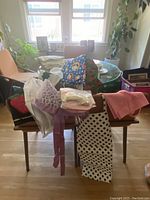 Photo of 11 aprons laid over chairs showing various colors and patterns, including polka dots, pastel pink, and colorful prints.