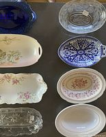 Top-down view of eight serving pieces including glass trays and ceramic plates with various floral and geometric patterns
