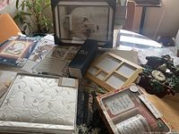 Top view of lot featuring throw blanket, cross stitch patterns, frames, mug set, wedding album, cuckoo clock planter, and part of tapestry.