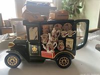 Photo of the delivery truck teapot showing the left side with miniature tea sets, plates, and tea/coffee boxes attached, gold accents visible.