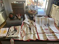 Overview of textiles including towels, apron, napkins, and tablecloth with rooster and chicken embroidery