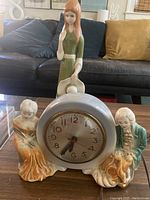Sessions electric mantel clock with colonial French style seated man and woman ceramic figures beside the clock face on a coffee table.
