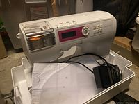 Brother CS-8150 sewing machine placed on case base, visible digital display, buttons, and power adapter along with instruction manual.