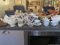 Overview shot displaying entire group of assorted teapots, teacups, creamers, and sugar bowls in various floral and decorative patterns on a kitchen countertop.