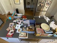 Wide photo of kitchen counter showing various boxes, cards, plates, and Christmas linens scattered on surface