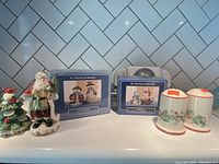 Four vintage Christmas salt and pepper shaker sets displayed on a tile counter, including two boxed sets and unboxed figurine shakers.