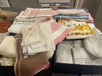 Photo showing an assortment of folded vintage linens and textiles including towels, napkins, pillowcases, and blankets with various patterns and colors.