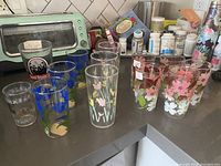 Set of 12 vintage glasses on kitchen counter showing multiple floral patterns and brewing logo glass