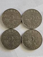 Four Canadian five cents coins from the 1930s showing denomination and maple leaf design.