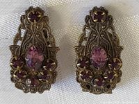 Full view of the pair of antique clip-on earrings with amethyst-colored stones, showing intricate filigree metalwork and the overall shape.