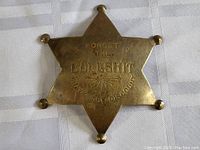 Photo of the large brass sheriff star badge showing the engraved humorous inscription: 'FORGET THE BULLSHIT WHAT'S THE DISCOUNT'.
