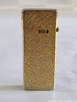 Front view of rectangular gold-tone textured pocket lighter with ignition wheel visible.