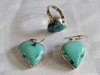 Photo showing the turquoise heart-shaped ring and matching earrings on a white textured fabric background.