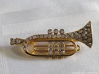 Close-up view of a vintage trumpet pin brooch with gold-tone metal and clear rhinestone decoration