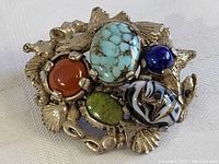 Close-up of vintage brooch pin showing multi-colored stones and detailed silver-toned sea life motif metal setting.