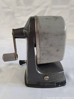 Side view of vintage pencil sharpener showing metal and plastic construction and hand crank