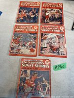 Top view of five vintage Enid Blyton's Sunny Stories children's books arranged on a white cloth, showing colorful illustrated covers and red borders.