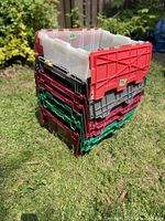 Stacked plastic storage totes in various colors showing wear and foldable lids for compact storage.