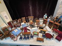 Wide shot showing entire lot of miniature furniture arranged on table, including chairs, tables, cabinets, and accessories.