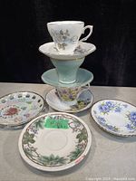 Photo of 3 teacups stacked with 8 extra saucers arranged around them showing floral designs and trims.